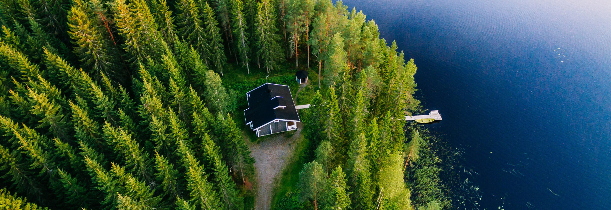 Aerial view of wooden cottage in green forest by the blue lake in rural summer Finland Aerial view of wooden cottage in green pine forest by the blue lake in rural summer Finland