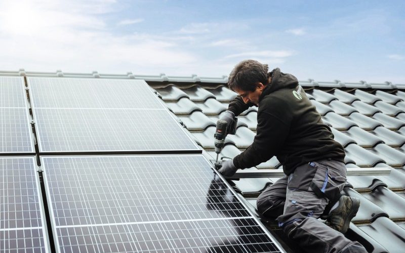 Handwerker bei der Montage eines Solarmoduls auf Hausdach