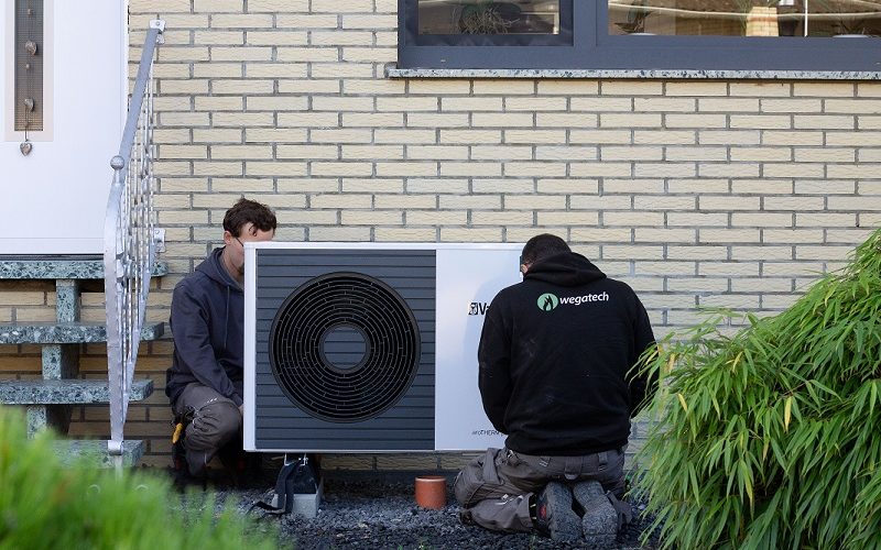 Heizungsinstallateure der Firma Wegatech bauen Wärmepumpe vor Haus ein