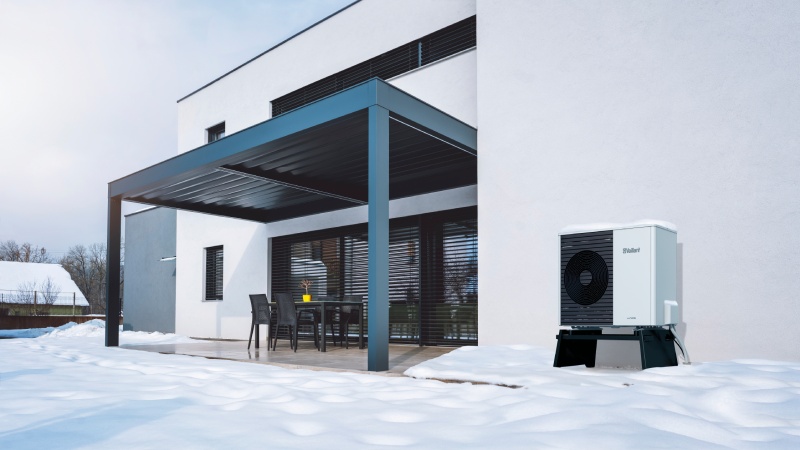Kaeltemittel Vaillant Wärmepumpe mit Schneehaube hinter modernem Haus im Winter