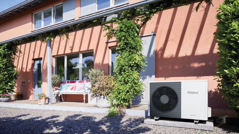 Vaillant Wärmepumpe hinter braunem Haus und neben Terrasse mit Rankpflanzen