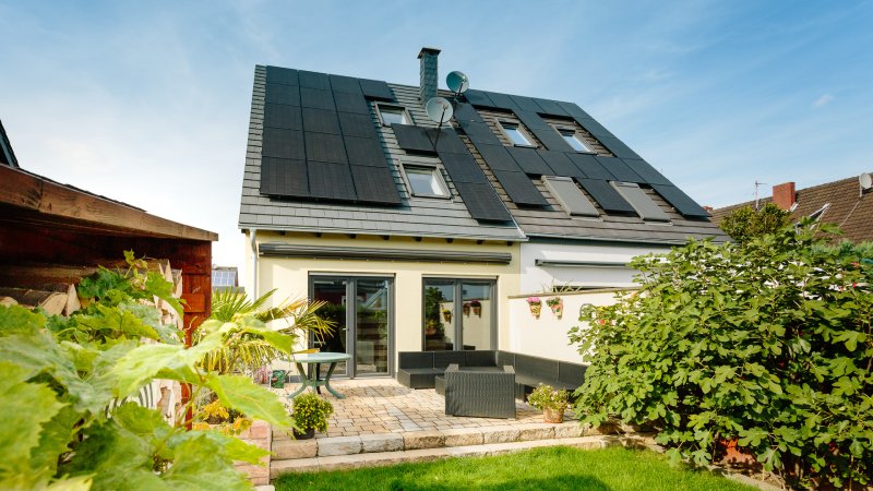Zweifamilienhaus mit All-Black-PV-Modulen auf dem Hausdach mit Garten und Terrasse im Vordergrund