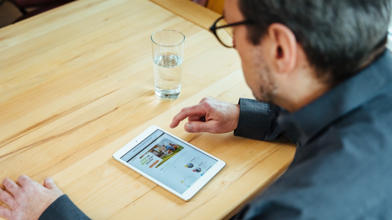 Mann arbeitet an seinem weißen Tablet an, welches auf Holztisch liegt