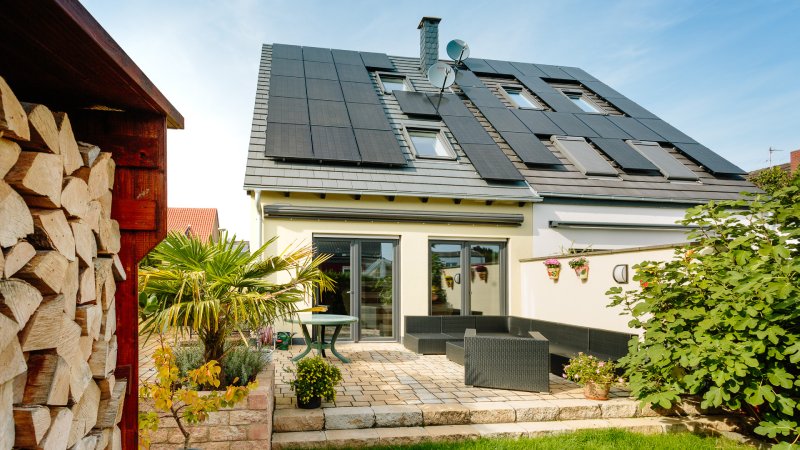 Modernes Zweiparteienhaus mit Photovoltaikanlage auf dem Dach und Garten mit Terrasse im Vordergrund