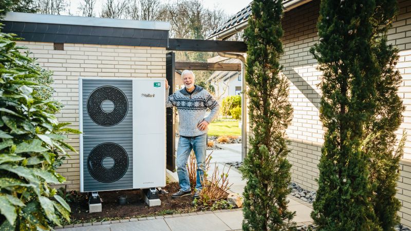 Mann neben Vaillant Wärmepumpe neben Haus mit Pflanzen im Vordergrund