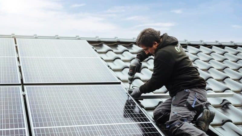 Handwerker bei der Montage eines Solarmoduls auf Hausdach