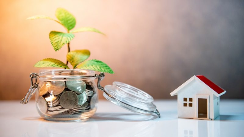 Photovoltaik_Investment Property or real estate investment. Home mortgage loan rate. Saving money for future concept. Reflection of green plant growing out of coins in glass jar and house model on the table