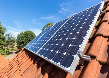 Row of solar panels on roof Row of blue solar panels on orange roof. Group of blue solar collectors with orange roof tiles. It's a photo of my own roof in the netherlands. In my country there is a enough sun to make electricity. The equipment stands on a steep flat roof with orange roof tiles. The panels have the same beautiful blue color as the sky. from the attic level you can view the street with trees on the ground.